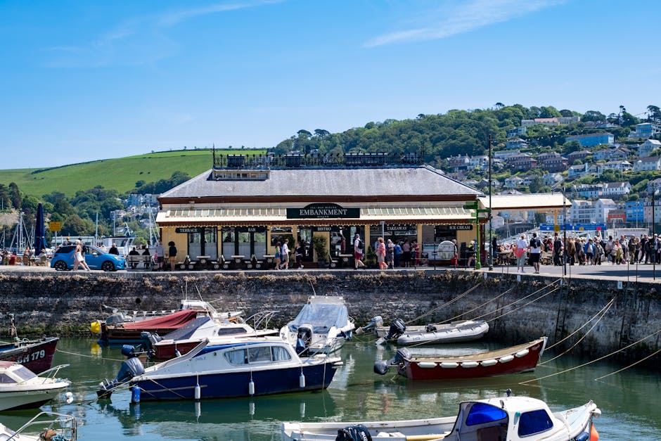 A panoramic view of a marina with numerous white motorboats and sailing yachts docked in calm waters, their masts rising vertically and some covered with protective fabric. The boats are moored along