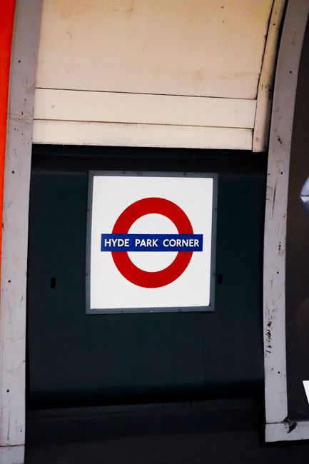 Inside the Green Park station on the London Underground, the curved tiled tunnel features metal train tracks running through the centre, with advertisements and station signage on the walls including 